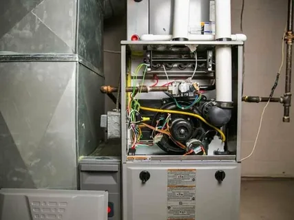 Open residential gas furnace showing internal components, wiring, blower motor, and control board inside an HVAC system.